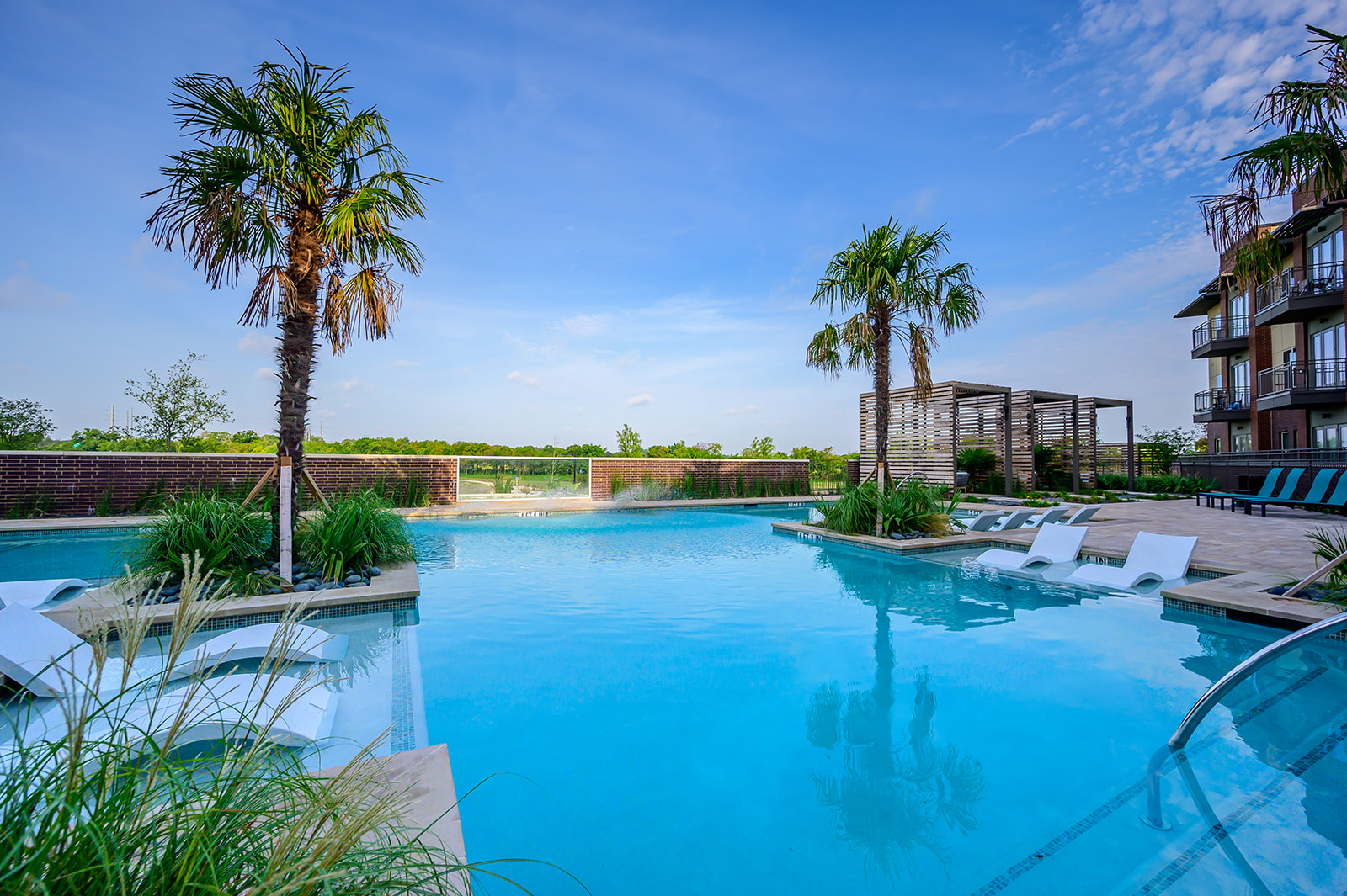 Luxury Apartments Garland- Massive Resort Style Pool With Submerged Lounge Chairs and Surrounding Palm Trees